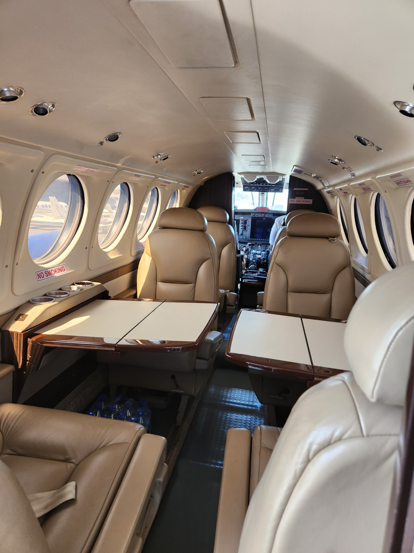 Beechcraft King Air B200 cabin with deployed tables and tan leather seating, cockpit visible